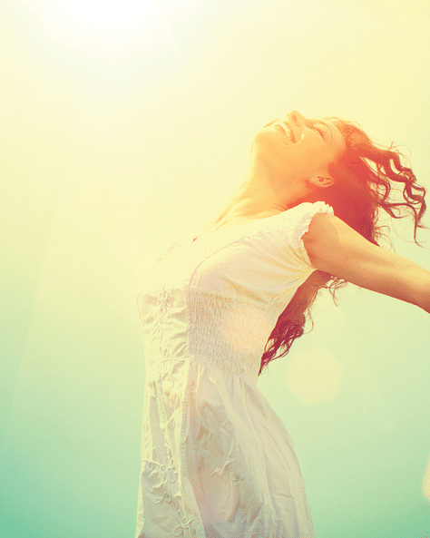 a woman standing with her hands wide apart enjoying the sun shining on her face